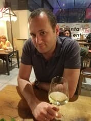 Man in a grey polo shirt holding a glass of white wine at a restaurant.